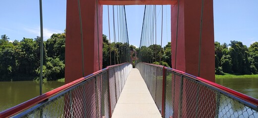 Hanging suspension bridge architecture made with iron metal cable rope and tower for crossing green forest river water. Empty and quiet endless deck, walkway or path close up view during daytime.