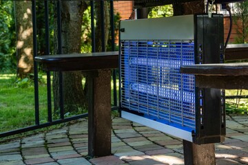 Ecosniper GC1-60 for destruction of flying insects,is installed under table in gazebo. Blurred...