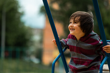 a three-year-old boy with long black hair swings on a swing in the playground, a happy child on a walk
