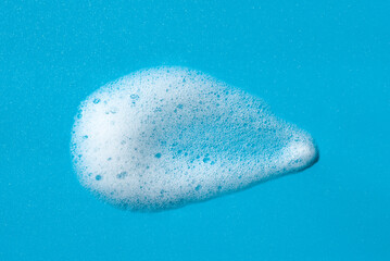 Obraz premium Foam swatch on a blue background. Soapy liquid texture with bubbles. Natural sunshine and shadows. Skin care cleansing cosmetic in top view.