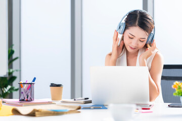 Asian businesswoman wearing headphones to listen to music in the office to relieve stress after work Listening to music made her happy and smiling.