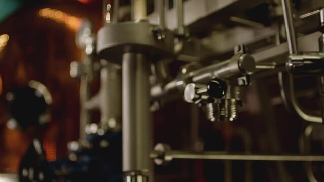Camera moving across metallic tubes inside alcohol drinks factory. Wine , vodka cognac distilling tanks . Metal taps or kegs for pouring alcohol . slow motion close-up . Row of chrome pipes in factory