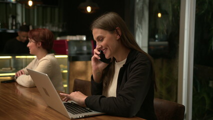 People inside coffee shop at night. Young millennial woman browsing internet online sitting at cafe