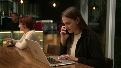 People inside coffee shop at night. Young millennial woman browsing internet online sitting at cafe