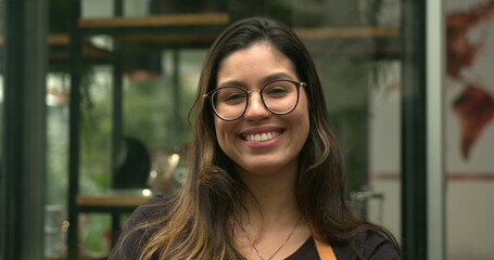 Portrait of young woman employee standing in front of coffee shop smiling at camera