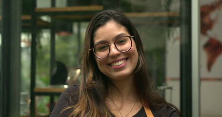 Portrait of young woman employee standing in front of coffee shop smiling at camera