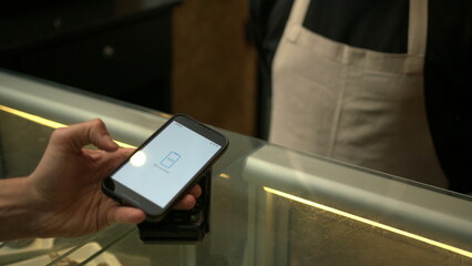 Customer paying with contactless NFC payment technology on smartphone device inside business store