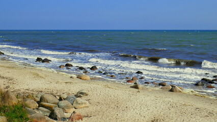 Fototapeta na wymiar Strand der Ostsee auf der Insel Fehmarn mit Wellen, Sand und großen Kieselsteinen unter blauem Himmel