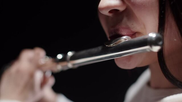 Closeup musician's female lips to which brings flute and plays music, dark background in studio. Female musician plays flute. Concept musical instrument