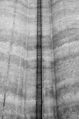 A ladder leading up a concrete wall of a factory silo.