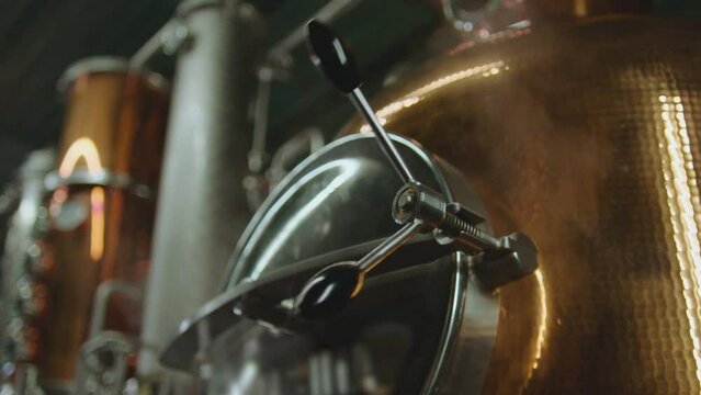 Professional big factory of alcohol drinks . Man's hand opening door of tank . Vodka wine tequilla production filtration , distillation . Alcohol preparation . Close up making alcohol . Boiler , steam
