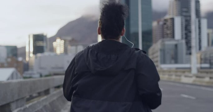 Rearview of an overweight woman city running along highway in outdoor workout. One active fit woman listening to music through earphones and jogging alone road. Losing weight and being healthy