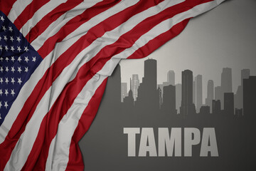 abstract silhouette of the city with text Tampa near waving national flag of united states of america on a gray background.