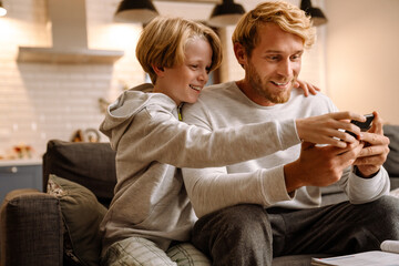 Obraz premium Ginger man using mobile phone while making fun with his son