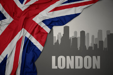 abstract silhouette of the city with text London near waving national flag of great britain on a...