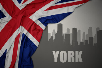 abstract silhouette of the city with text York near waving national flag of great britain on a gray...