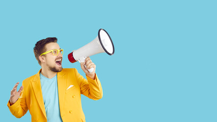 Wide banner of excited young man isolated on blue studio background scream in megaphone about deal...