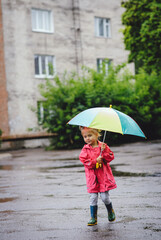 A little beautiful girl blonde, in boots and with umbrella walking along the puddles in the rain....