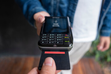 Person holding plastic credit card in hand, using terminal and paying for shopping