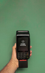 Credit or debit card terminal in hand isolated on green background. Close up of POS terminal in hand processing a pay. Copy Space