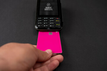 Person holding plastic credit card in hand, using terminal and paying for shopping