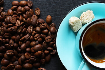 Photograph of roasted coffee beans and a blue cup of coffee with organic sugar cubes on a slate background for culinary illustrations - Powered by Adobe