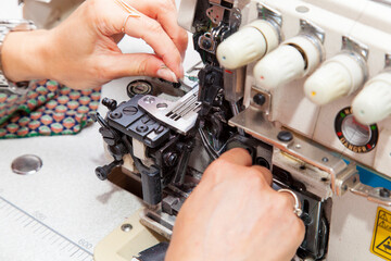 beautiful stylish woman designer inserts thread into overlock machine. hands close up