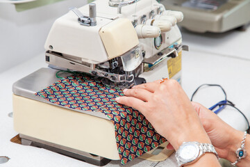 Beautiful young woman designer is working on an overlock machine. Hands close up