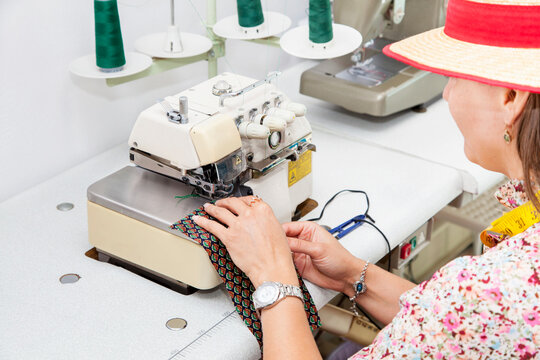 Beautiful young woman designer is working on an overlock machine