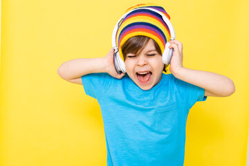 Handsome little boy in blue shirt and colorful hat with headphones, yellow background, banner