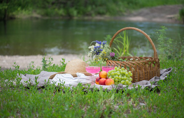 view of delicious snacks, fruits, lemonade and wine on the cover on green grass near the river.