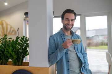 Fototapeta premium Man with cup smiling at camera standing indoors