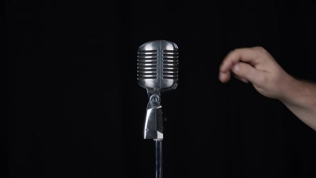 Turing on microphone and tapping it to test audio then turning it back off against black curtain.