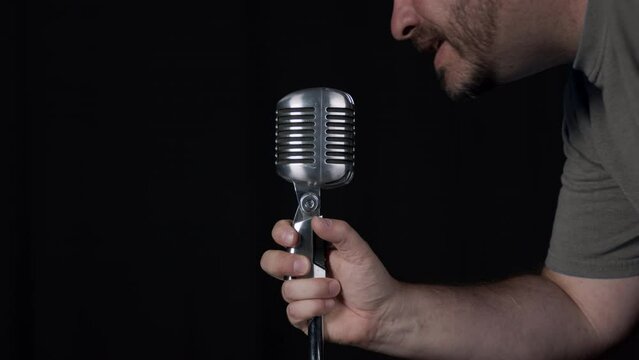 Person turning on and testing microphone and speaking into it against black background.