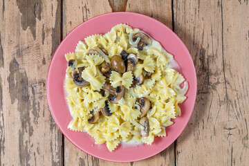 Farfalle pasta in a creamy sauce with champignon mushrooms in a plate on a wooden table.
