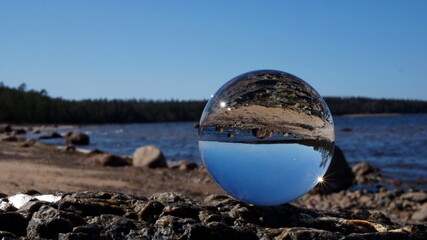 Fototapeta na wymiar Coast of the Gulf of Finland. Crystal ball in the foreground and the beach, rocks, sea and pine forest on the horizon. Leningrad region, Russia.