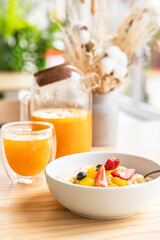 Healthy breakfast in a cafe with oatmeal porridge with berries, banana and mango in bowl and spicy sea buckthorn tea on wooden table. Modern minimal scandinavian interior.