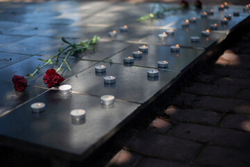Candles on gravestone. Wax candles burn on war monument. Two flowers on tombstone. Burial place of soldiers.