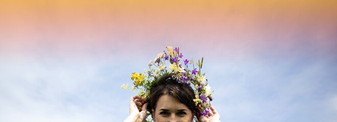 A pretty girl holds a wreath of flowers with her hands. Summer solstice concept. Place for text - obrazy, fototapety, plakaty