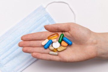 pills in a female hand and a blue medical mask on a white background