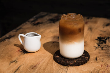 Cold iced latte coffee in the making. A tall highball glass filled with ice cubes and refreshing drink, a milk jug, copy space