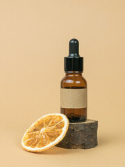 A bottle with an eyedropper on an old tree and a dried orange on a beige background. Cosmetics and medicinal products based on natural minerals.