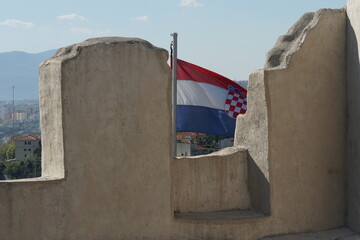 Croatian flag flapping behind the stone wall of trsat castle in town of Rijeka in Croatia. behind...
