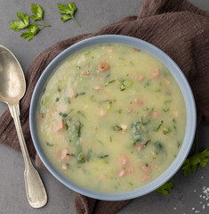 Traditional portuguese green soup with potato, green cabbage and sausage in a bowl over stone background