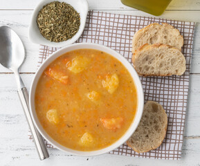 Vegetable soup in a bowl with seasonings and bread slices over wooden table