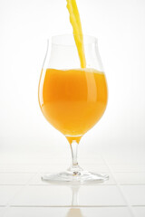 Orange juice pouring into drinking glass on white background. Shallow depth of field