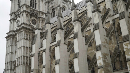 View from the bottom on the Westminster Abbey exterior details against the grey cloudy sky. Action. It is a large, mainly Gothic abbey church in the City of Westminster, London