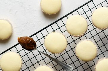 Three cornstarch alfajores with coconut and a spoonful of dulce de leche on white background. 