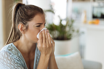 Young woman blowing her nose with a tissue at home