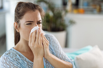 Young woman blowing her nose with a tissue at home
